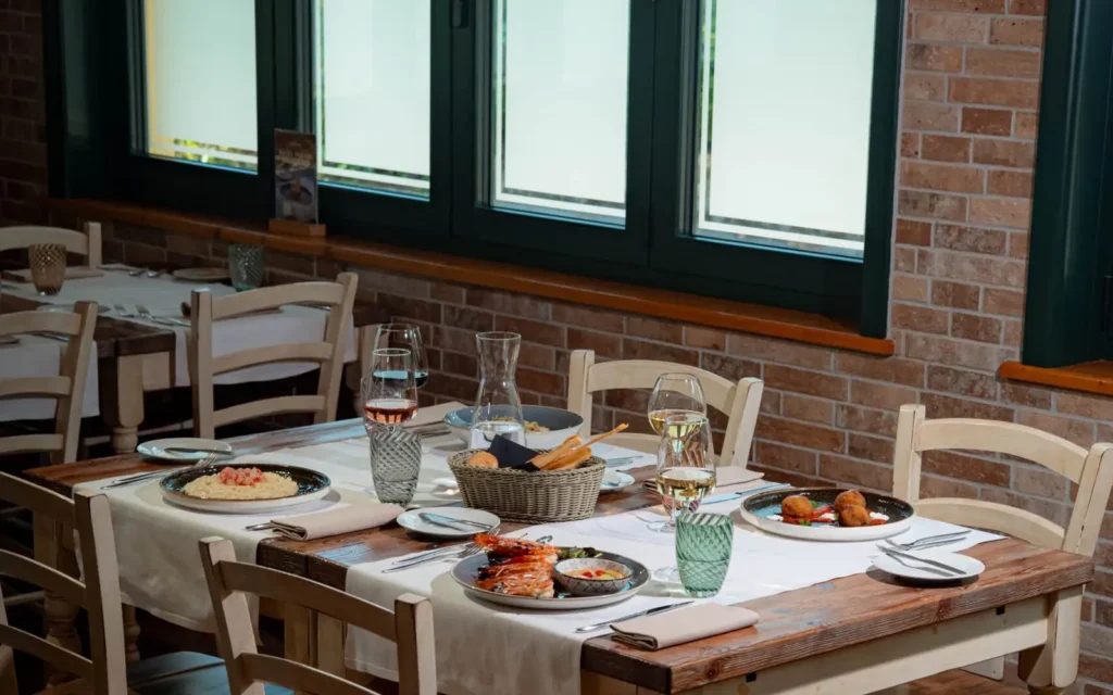 Un tavolo apparecchiato nella sala del ristorante Villa Giglio, vicino alle finestre, con piatti, pane e vino